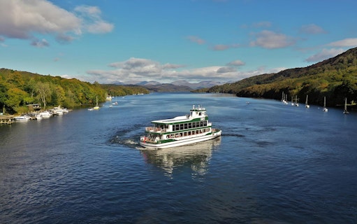 Cruise boat on Lake District waters with scenic hills, part of a day tour from London.