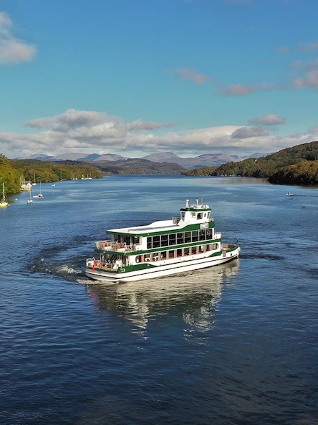 Cruise boat on Lake District waters with scenic hills, part of a day tour from London.