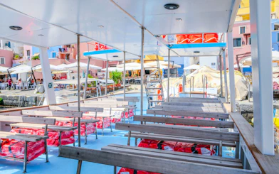 Boat deck with seating, docked at Procida Island, colorful buildings and cafes in the background.