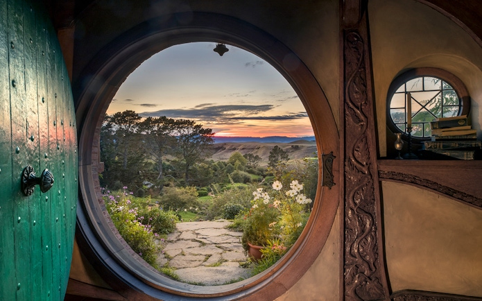 View from Hobbiton Movie Set door at sunset, featuring gardens and distant hills, New Zealand.