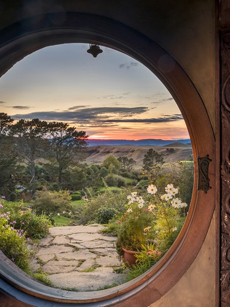 View from Hobbiton Movie Set door at sunset, featuring gardens and distant hills, New Zealand.
