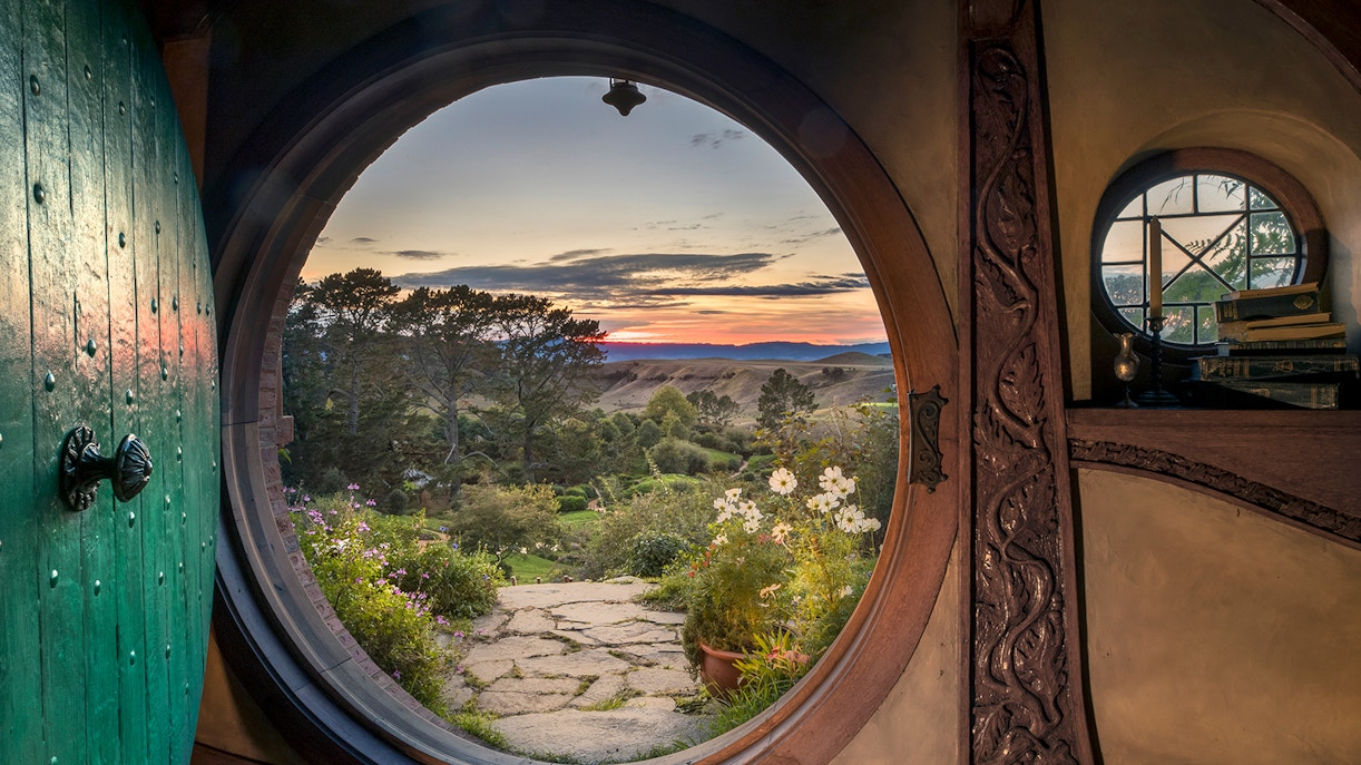 View from Hobbiton Movie Set door at sunset, featuring gardens and distant hills, New Zealand.