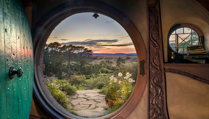 View from Hobbiton Movie Set door at sunset, featuring gardens and distant hills, New Zealand.
