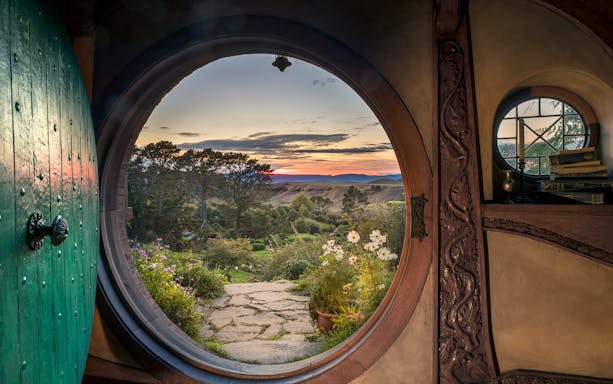 View from Hobbiton Movie Set door at sunset, featuring gardens and distant hills, New Zealand.