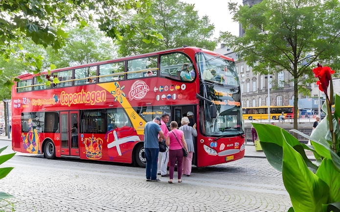 Tourists boarding a red hop-on hop-off bus in Copenhagen.