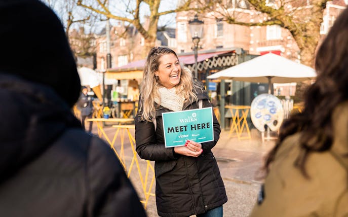 Tour guide holding a "Meet Here" sign in Amsterdam for food and history tour.