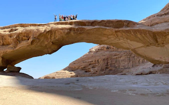 Group on rock bridge in Wadi Rum desert during Amman to Petra tour.