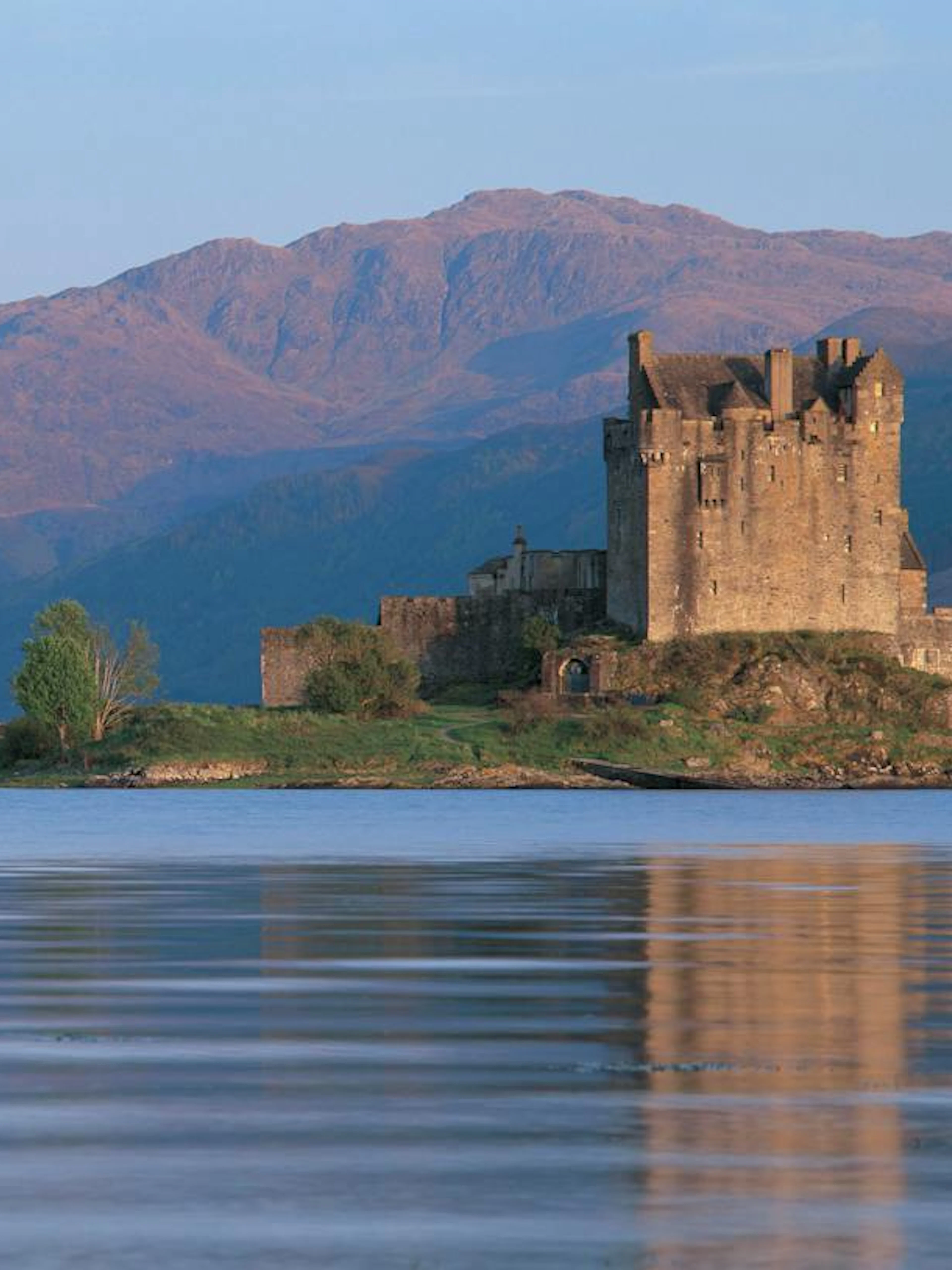 Eilean Donan Castle on a small island with a stone bridge, surrounded by mountains and water, Scotland.