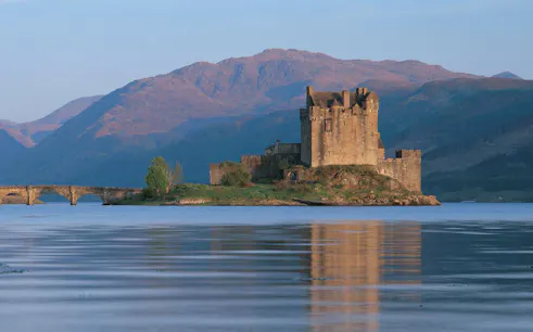 Eilean Donan Castle on a small island with a stone bridge, surrounded by mountains and water, Scotland.