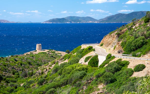 Coastal road and ancient tower along Alghero coastline during e-bike tour.