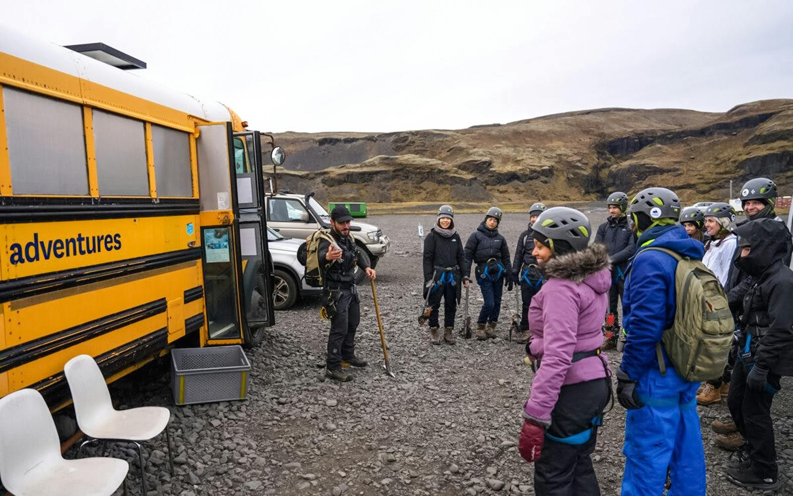 Tour guide briefing group before Blue Ice Glacier Hike near yellow bus in Iceland.