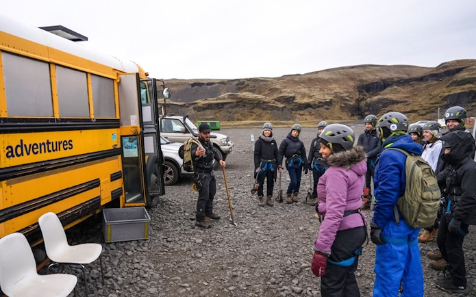 Tour guide briefing group before Blue Ice Glacier Hike near yellow bus in Iceland.