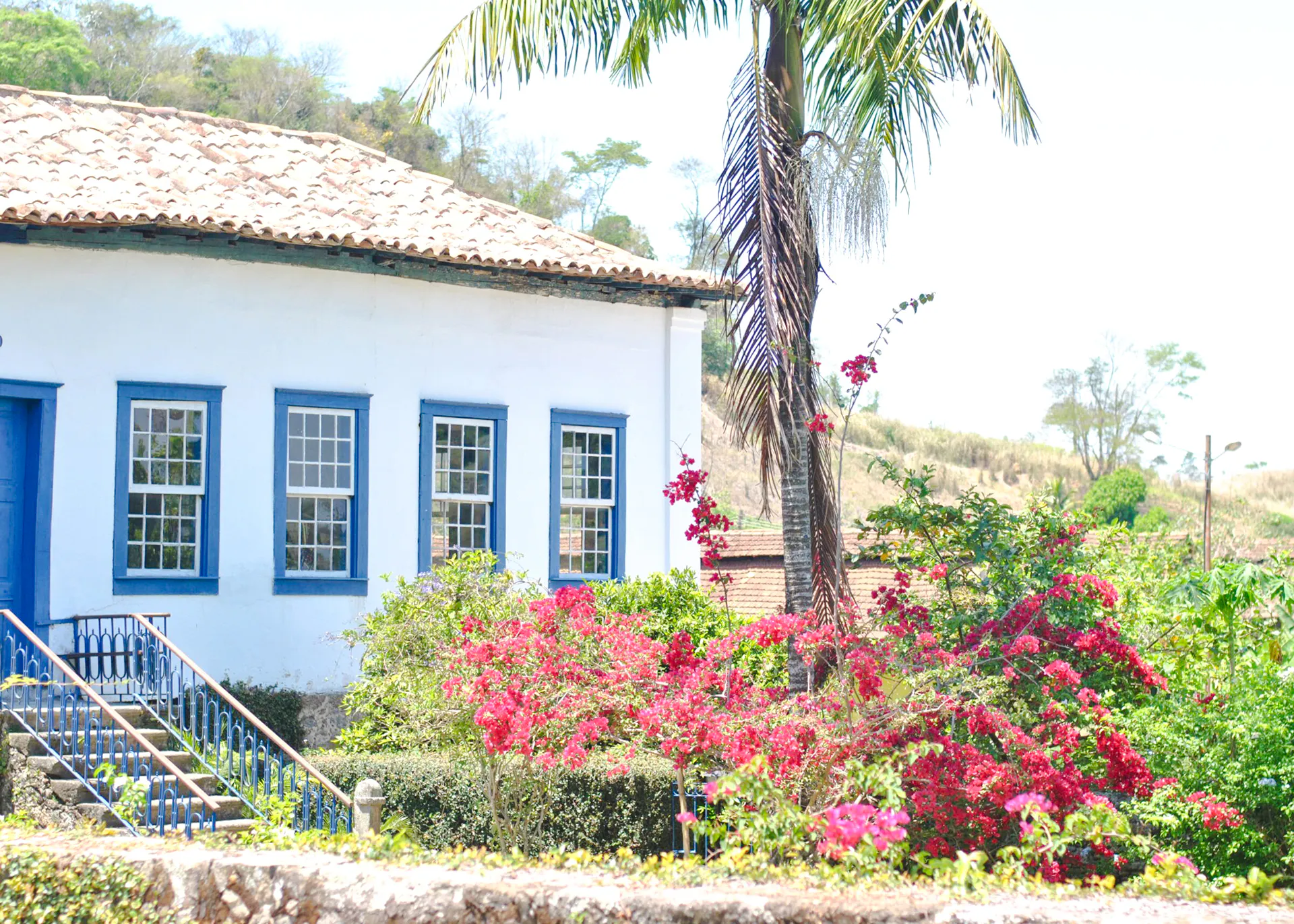Colonial house with blue trim surrounded by vibrant flowers in Coffee Valley, Rio de Janeiro.