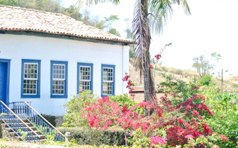 Colonial house with blue trim surrounded by vibrant flowers in Coffee Valley, Rio de Janeiro.