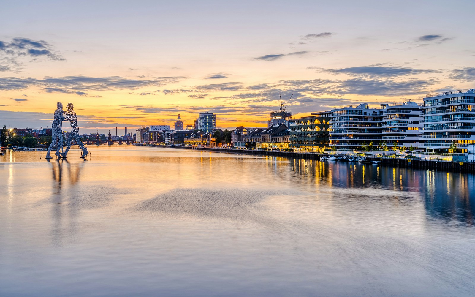 Sunset over the River Spree in Berlin with Molecule Man sculpture and city skyline.