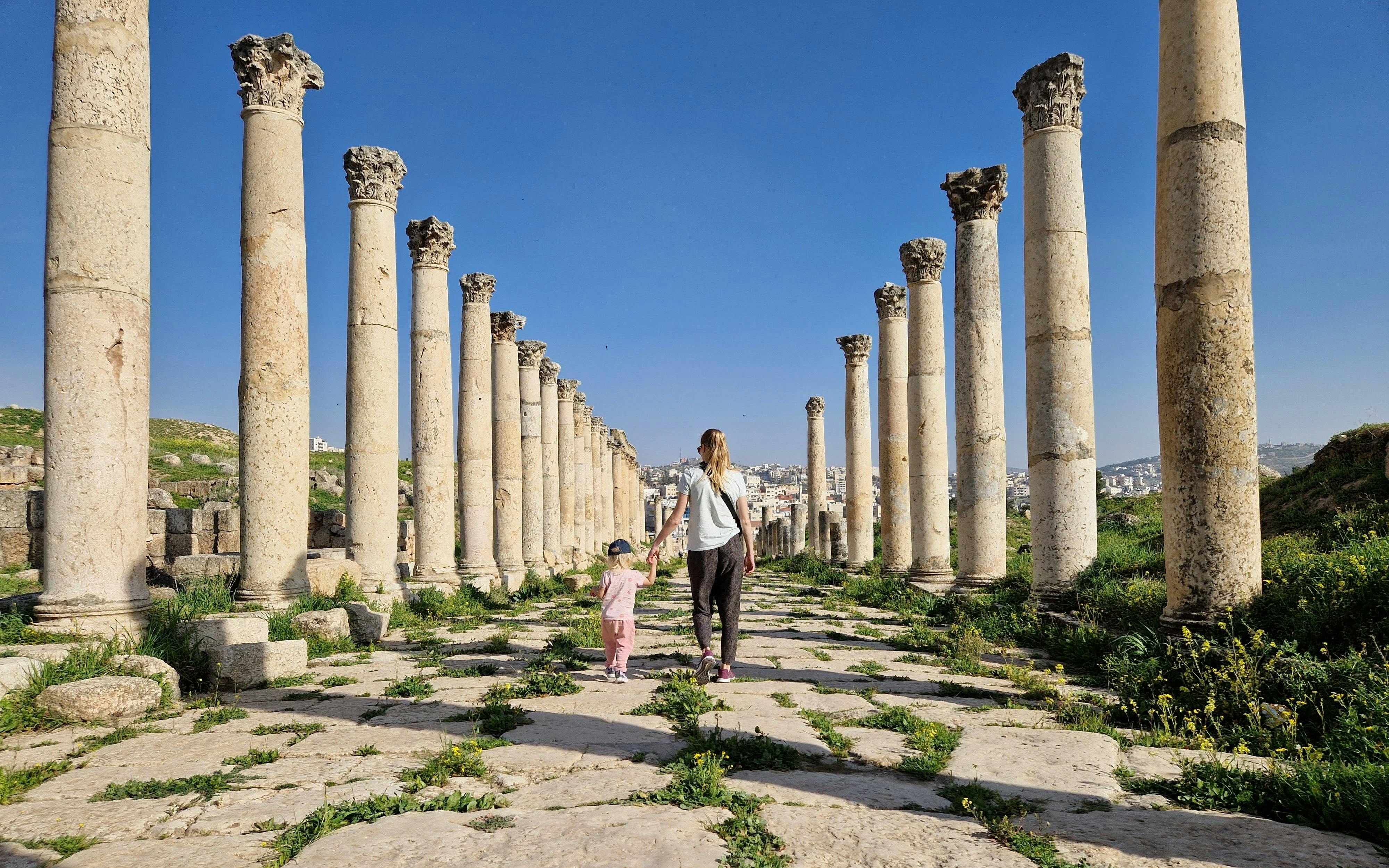 Mother and child walking through ancient columns in Jerash, Jordan.