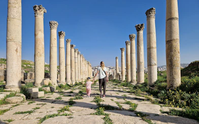 Mother and child walking through ancient columns in Jerash, Jordan.