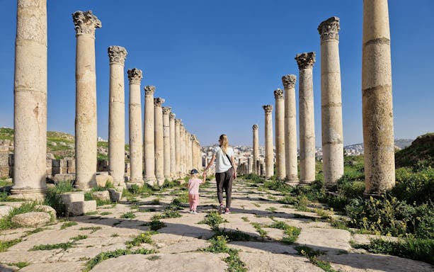 Mother and child walking through ancient columns in Jerash, Jordan.