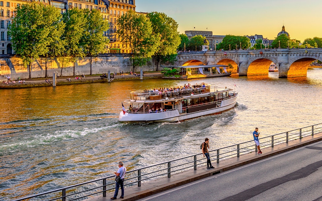 Seine River cruise boat passing under a bridge in Paris, France at sunset.