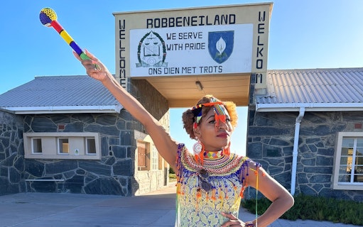 Guide in traditional attire at Robben Island prison entrance, South Africa.
