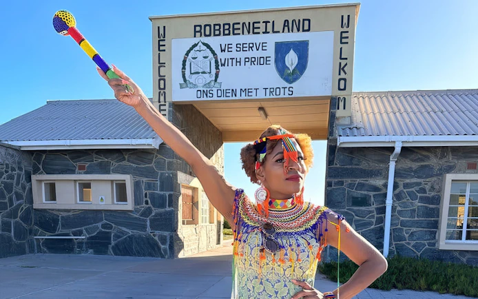 Guide in traditional attire at Robben Island prison entrance, South Africa.