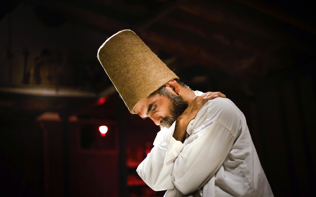Whirling Dervish in traditional attire performing in a dimly lit setting.