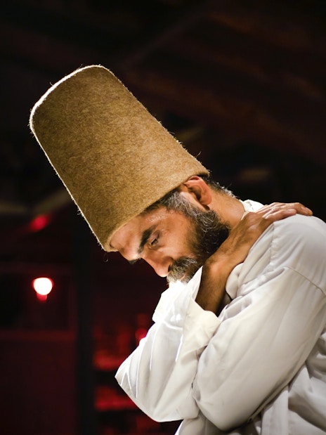 Whirling Dervish in traditional attire performing in a dimly lit setting.