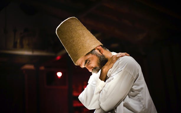 Whirling Dervish in traditional attire performing in a dimly lit setting.