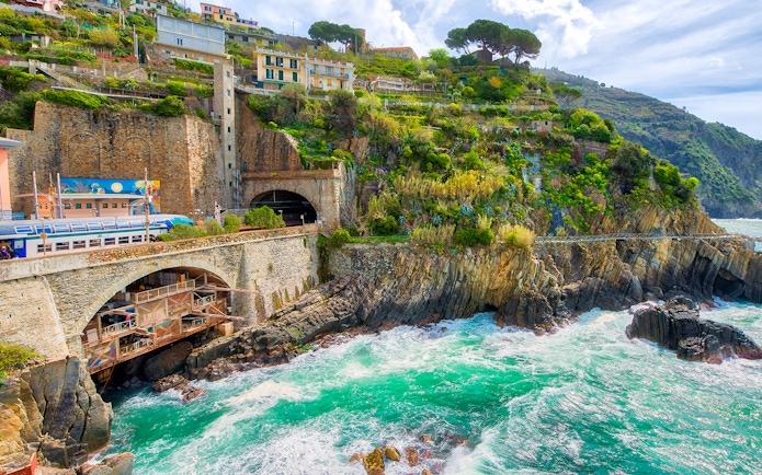 Train passing through coastal cliffs in Cinque Terre, Italy, with colorful hillside houses.