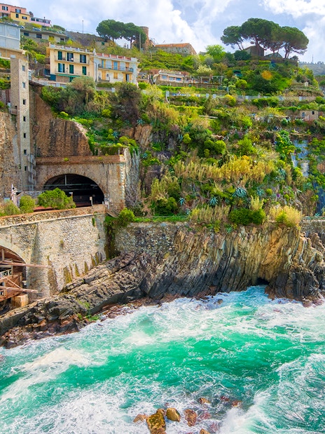 Train passing through coastal cliffs in Cinque Terre, Italy, with colorful hillside houses.
