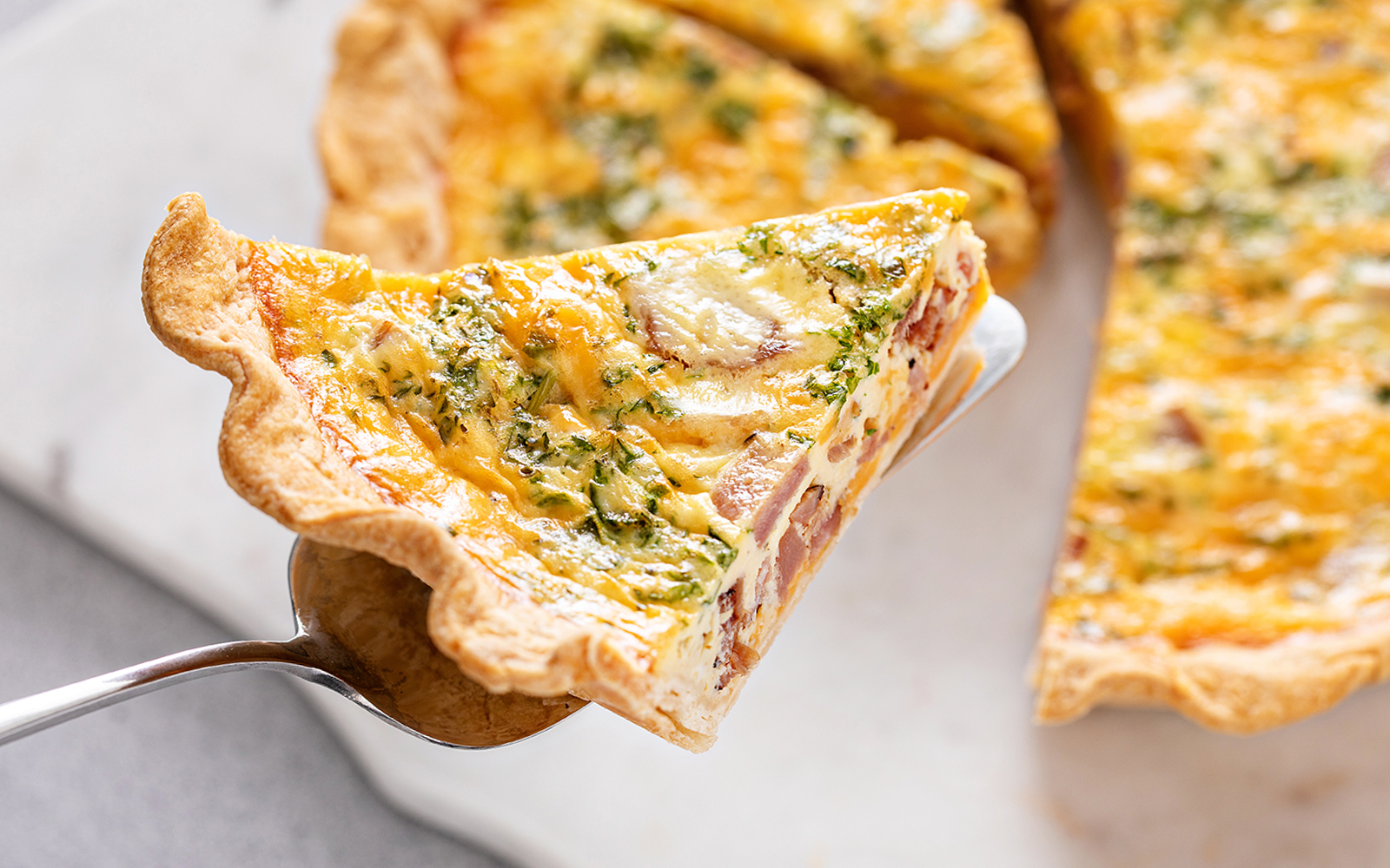 Slice of Quiche Lorraine with ham and herbs on a serving spatula.