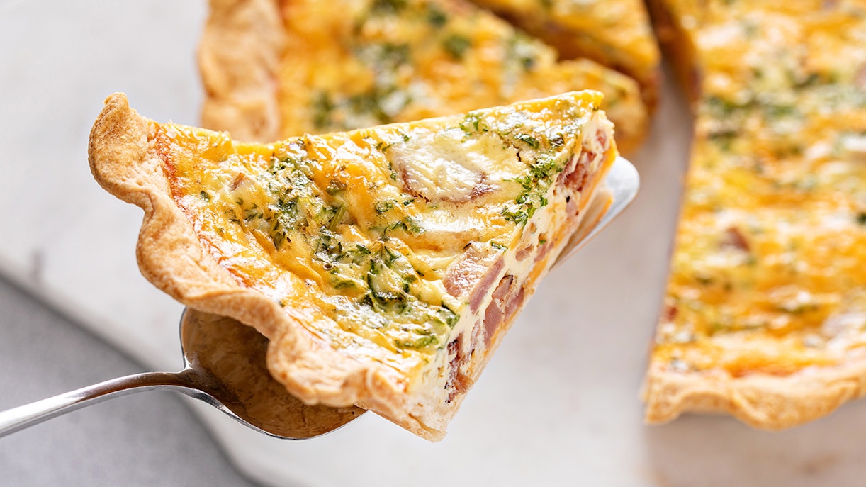 Slice of Quiche Lorraine with ham and herbs on a serving spatula.