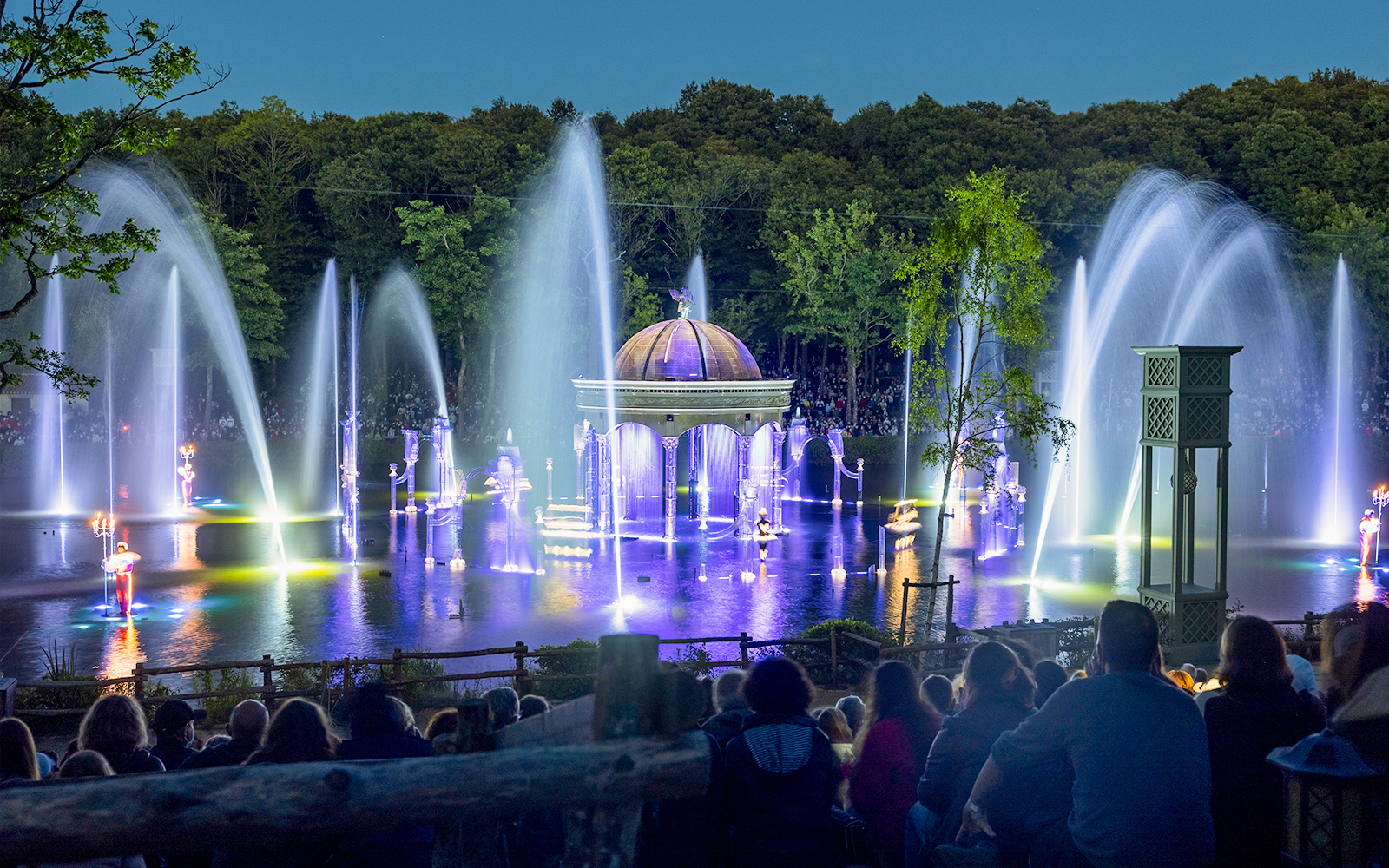 Nighttime fountain show at Puy du Fou with illuminated water jets and audience.