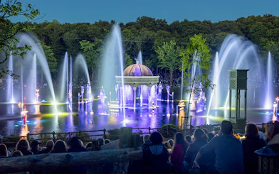 Nighttime fountain show at Puy du Fou with illuminated water jets and audience.