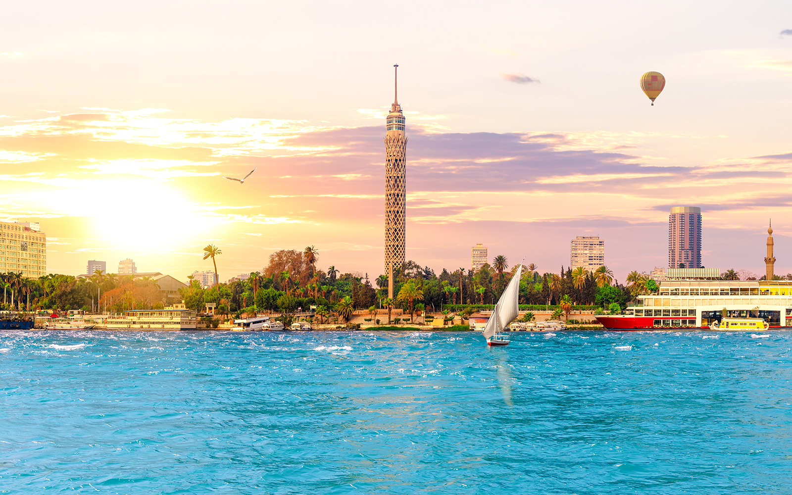Cairo skyline with Nile River, sailboat, and hot air balloon at sunset, Egypt.