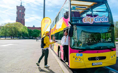 Guests boarding City Circle Bus in Berlin near historic building.