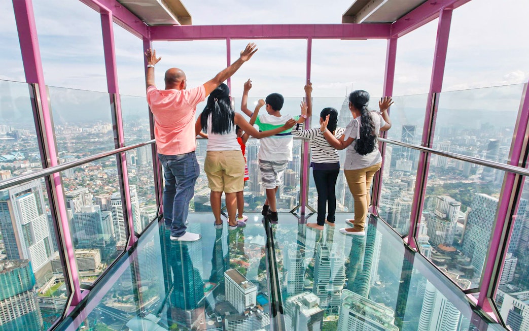 Visitors standing on the KL Tower SkyBox glass floor overlooking Kuala Lumpur skyline.