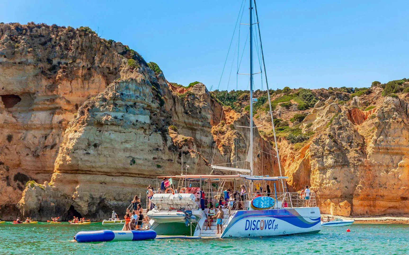 Tourists on a catamaran enjoying inflatable water activities near Ponta da Piedade, Lagos.