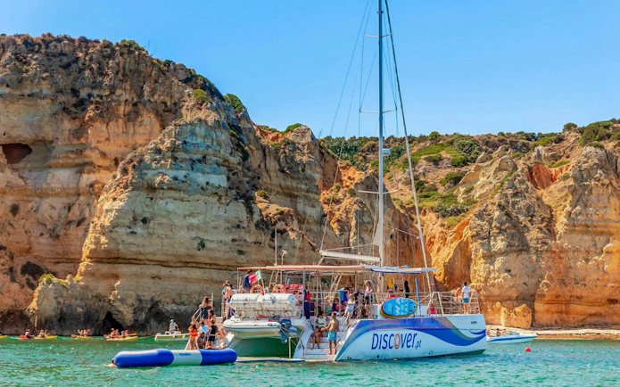 Tourists on a catamaran enjoying inflatable water activities near Ponta da Piedade, Lagos.
