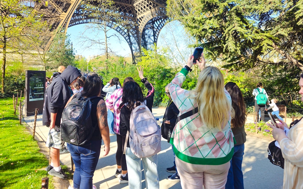 Tourists gather under the Eiffel Tower in Paris, France, capturing photos and enjoying the view.