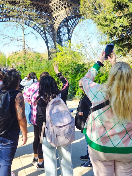 Tourists gather under the Eiffel Tower in Paris, France, capturing photos and enjoying the view.