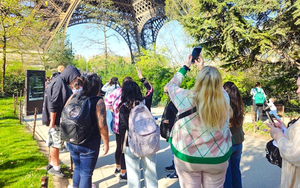 Tourists gather under the Eiffel Tower in Paris, France, capturing photos and enjoying the view.