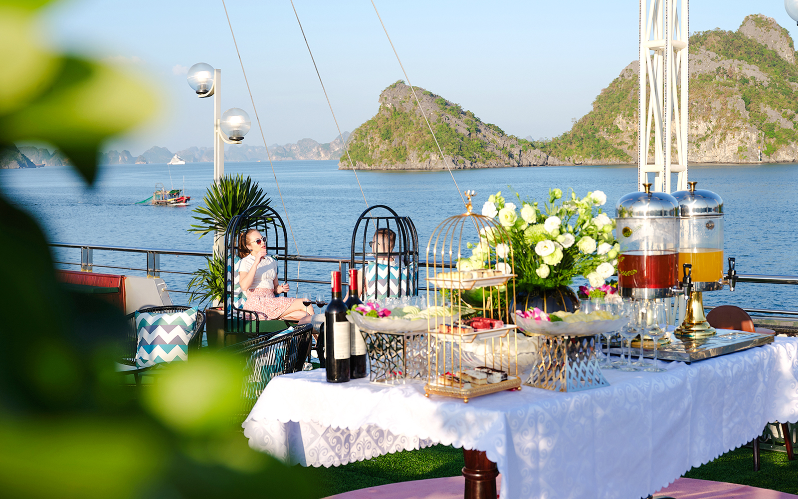 Couple enjoying drinks on cruise ship deck with Ha Long Bay islands in background.