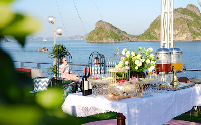 Couple enjoying drinks on cruise ship deck with Ha Long Bay islands in background.