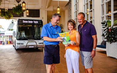 Tour guide showing itinerary to couple in front of Down Under Tours coach.