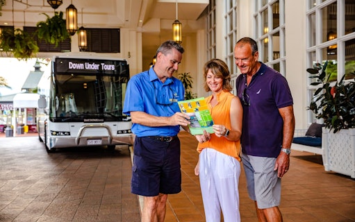 Tour guide showing itinerary to couple in front of Down Under Tours coach.