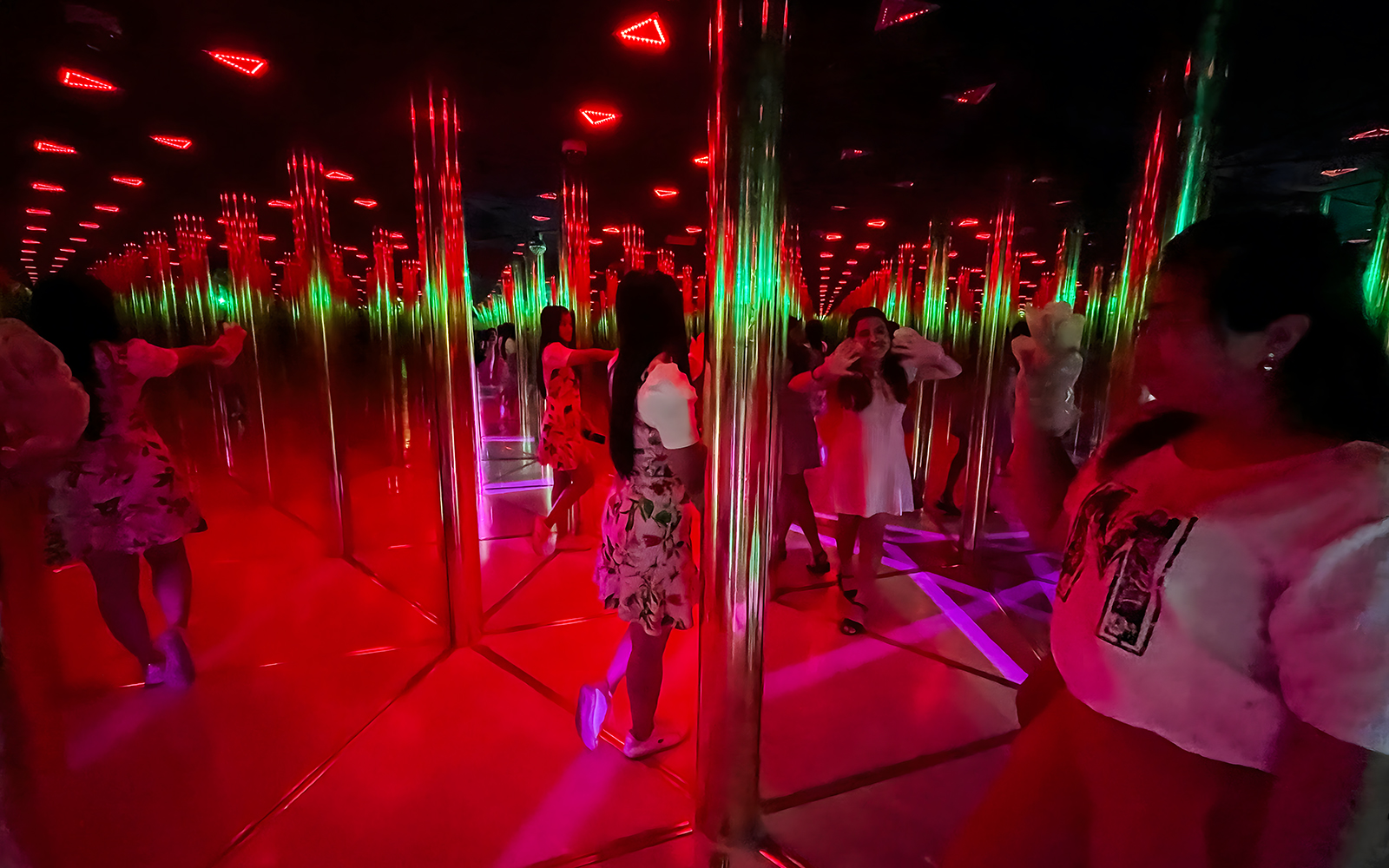 Tourists exploring a colorful mirror maze with reflections and lights.