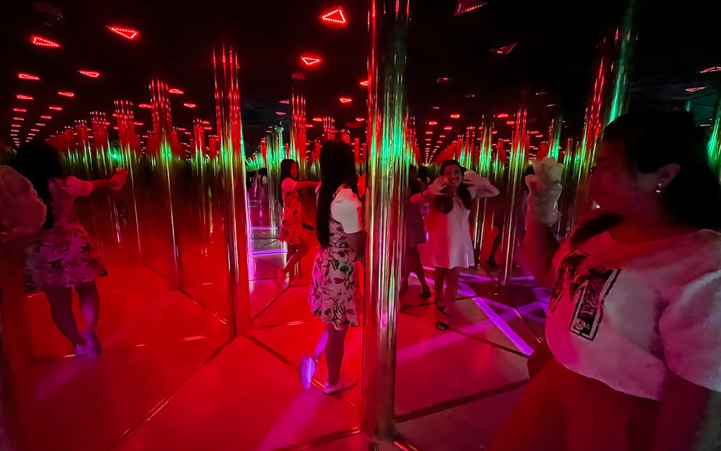 Tourists exploring a colorful mirror maze with reflections and lights.