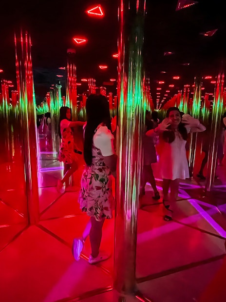 Tourists exploring a colorful mirror maze with reflections and lights.