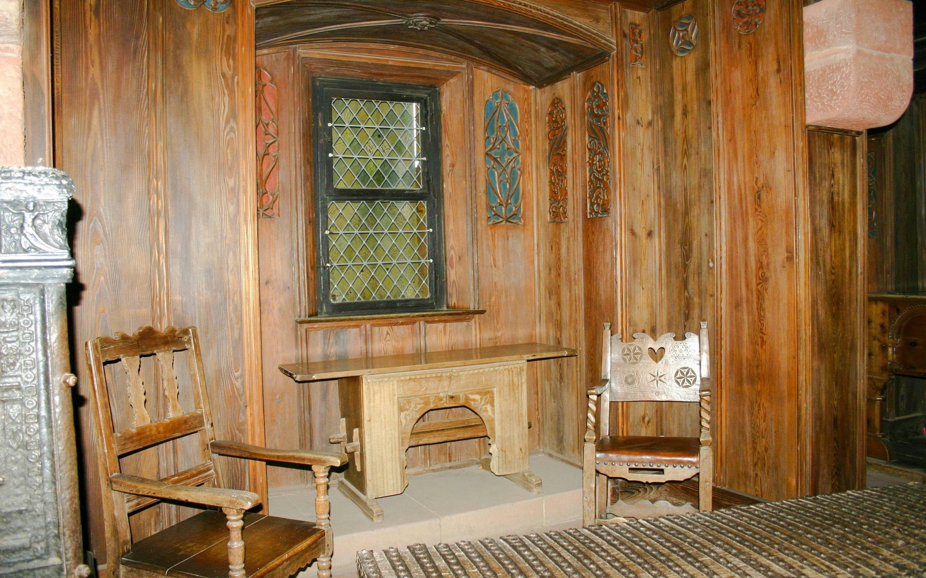 Interior of Haut-Koenigsbourg Castle with wooden chairs and ornate window.